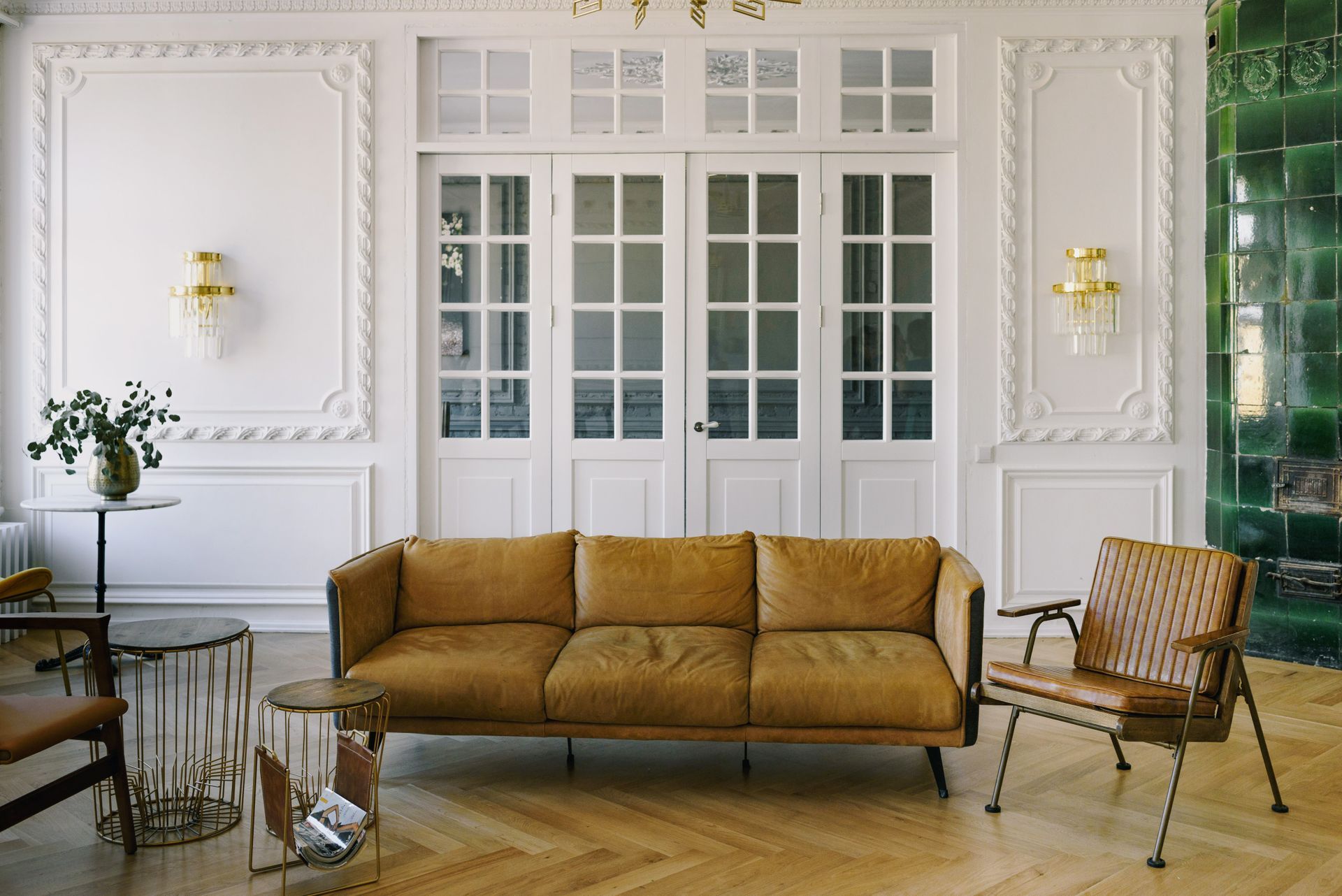 Salon aux murs blancs moulurés, canapé en cuir camel et parquet en point de Hongrie